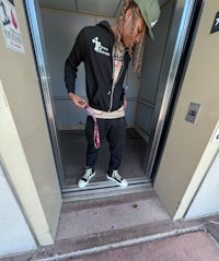 a man standing in an elevator wearing a hoodie and sneakers